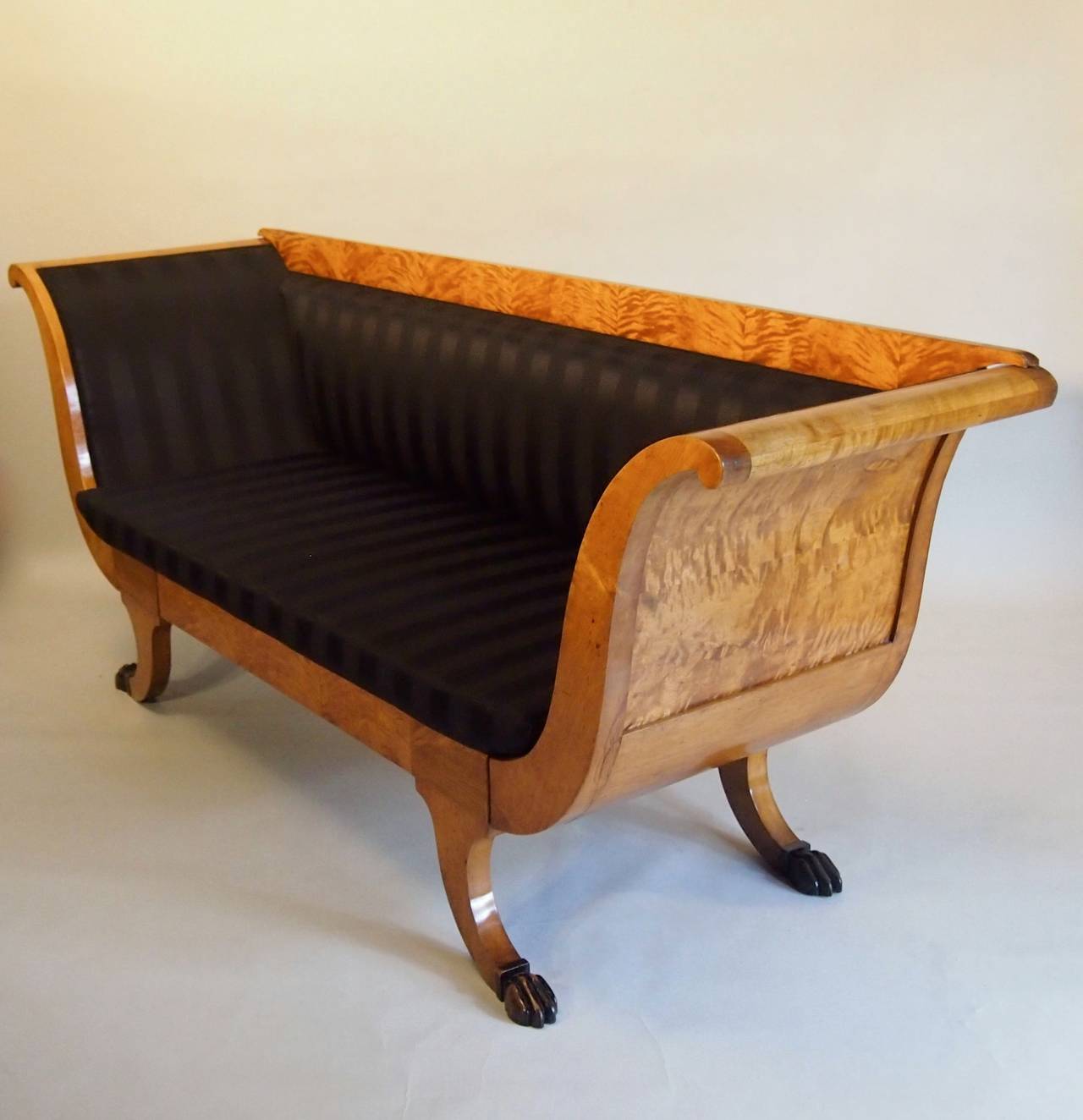 Flame birch Swedish Biedermeier sofa with solid side panels. The feet have been decorated with hand-carved ebonised lions paw feet. Reupholstered in a black on black Tricia gild fabric. This is a very elegant sofa with lovely proportions.