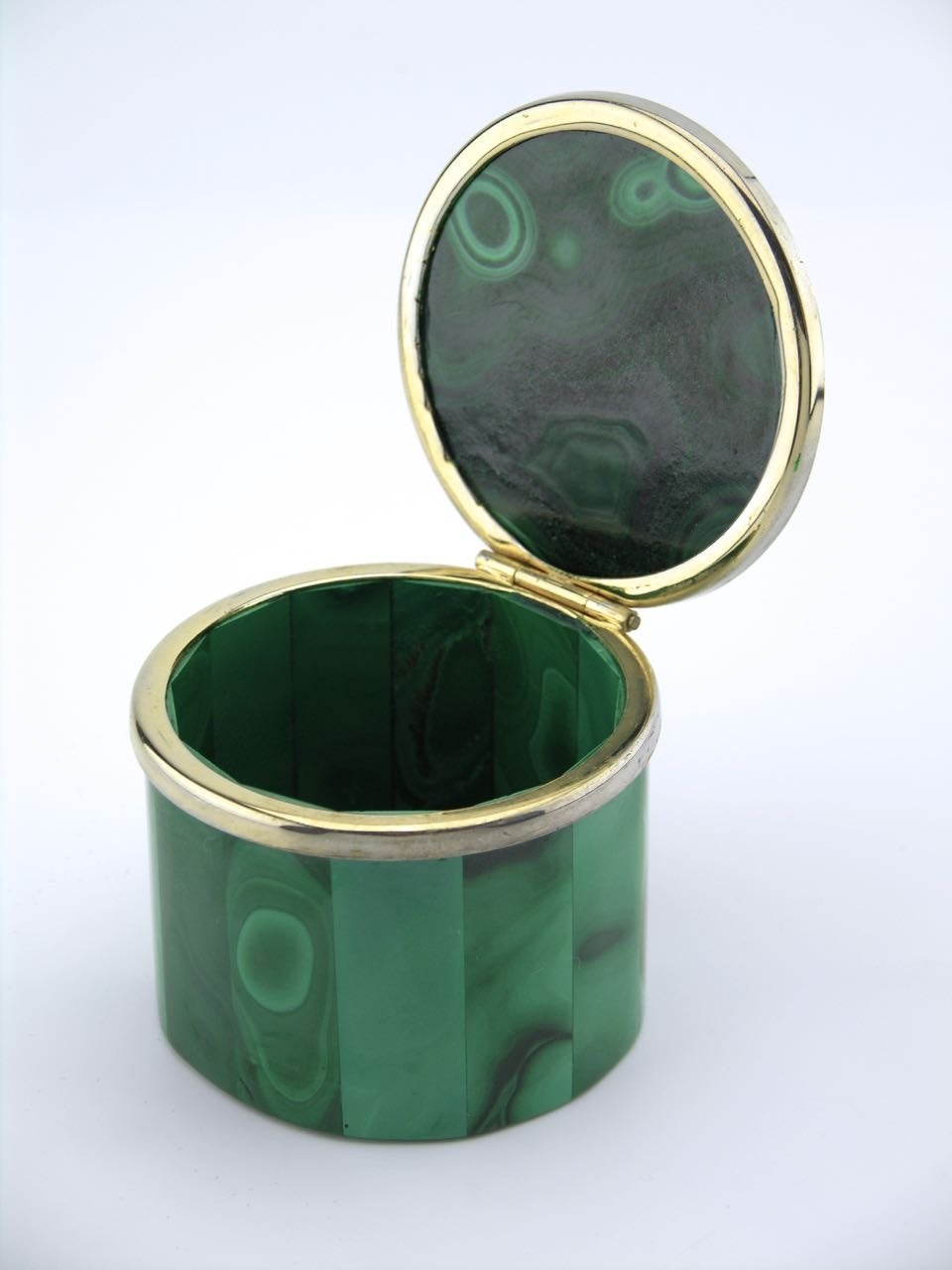 A cylindrical table box featuring a large thick cabochon panel of bulls eye malachite in the lid. The faceted base made of small panels of malachite arranged edge to edge.

A gold plated metal hinge and rim to the top.