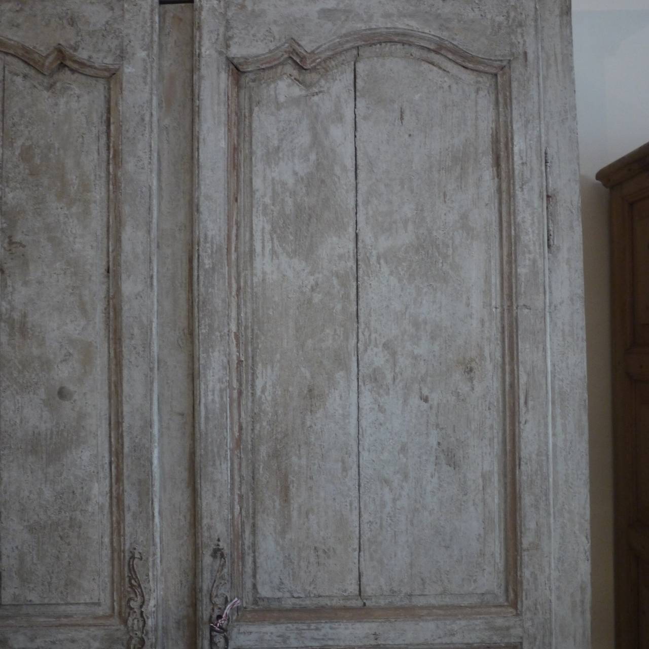 An early painted French Provincial Oak armoire, with arched panels to the doors and fitted shelves in the interior, weathered grey painted finish.