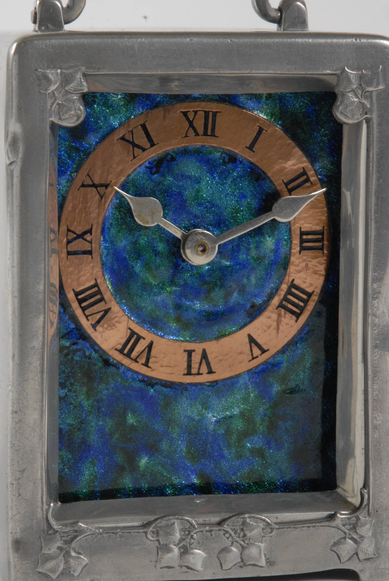 A Liberty & Co. carriage clock designed by Archibald Knox, circa 1903, pewter, copper and enamel. A French movement with fixed winder.
Copper chapter ring with black Roman numerals, pewter minute and hour hands on a large blue or green slab of