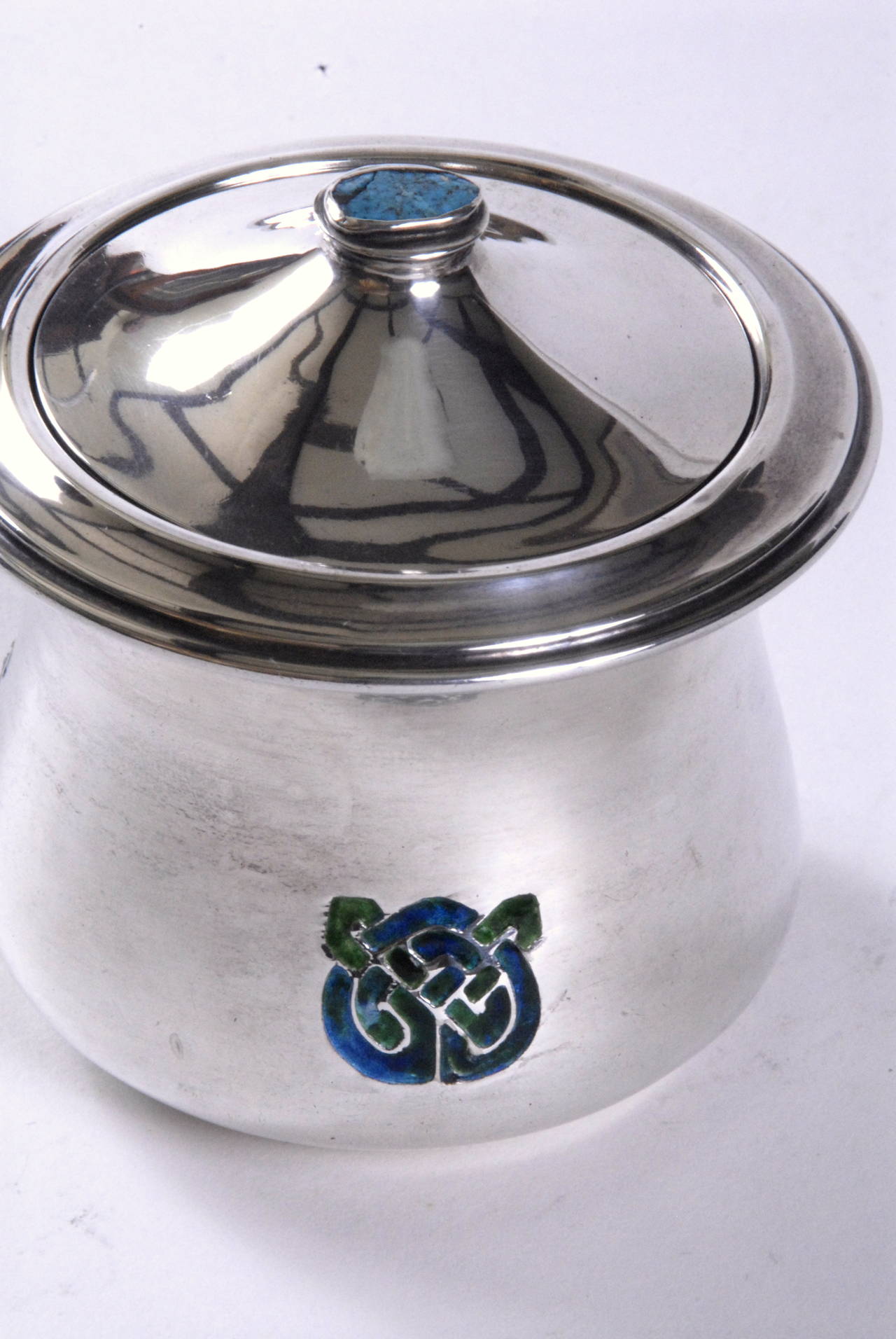 A silver covered bowl by Liberty, London designed by Archibald Knox. Hall marked underneath for L&Co Birmingham, 1902. CYMRIC.
The waisted body has 3 blue/green enamelled Celtic designs spaced around it and the lid knop is fitted with a piece of