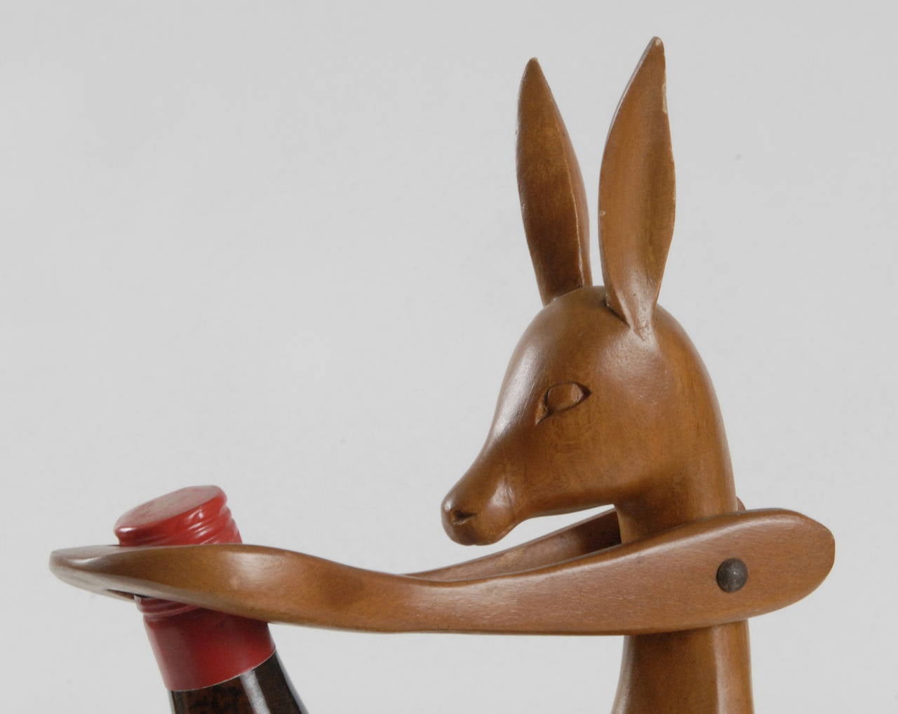 A carved wooden kangaroo bottle holder or pourer. Dating from the 1950s this has been carved from one piece of timber with the upper arms hinged to hold the bottle and rise to allow removal.
