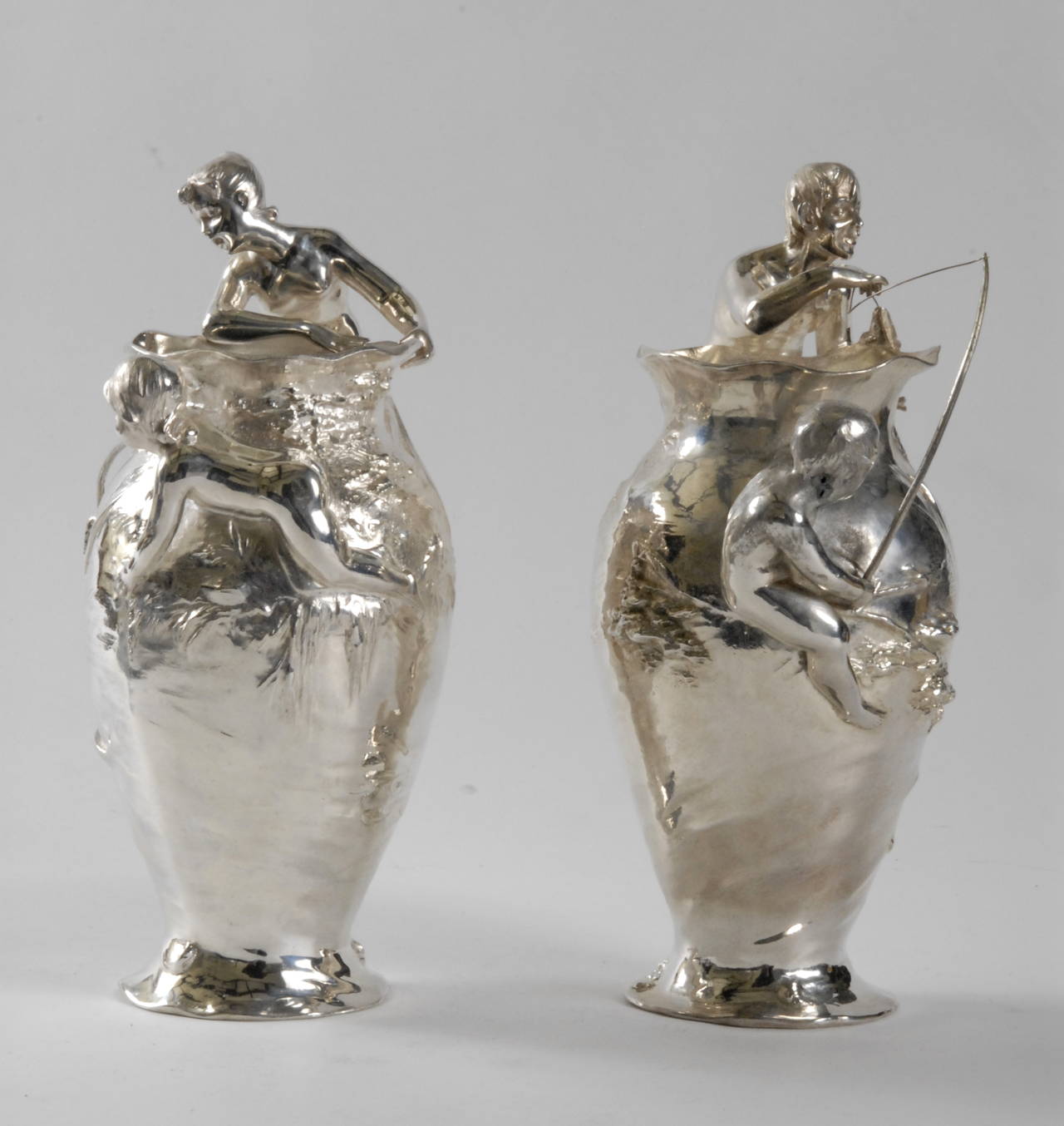 A pair of WMF [Wurttembergische Metallwarenfabrik] flower vases decorated with a fisherman and fisherwoman with children. Silver plated pewter and high relief decoration. The vases have been re-plated and the fishing rods and lines are replacements