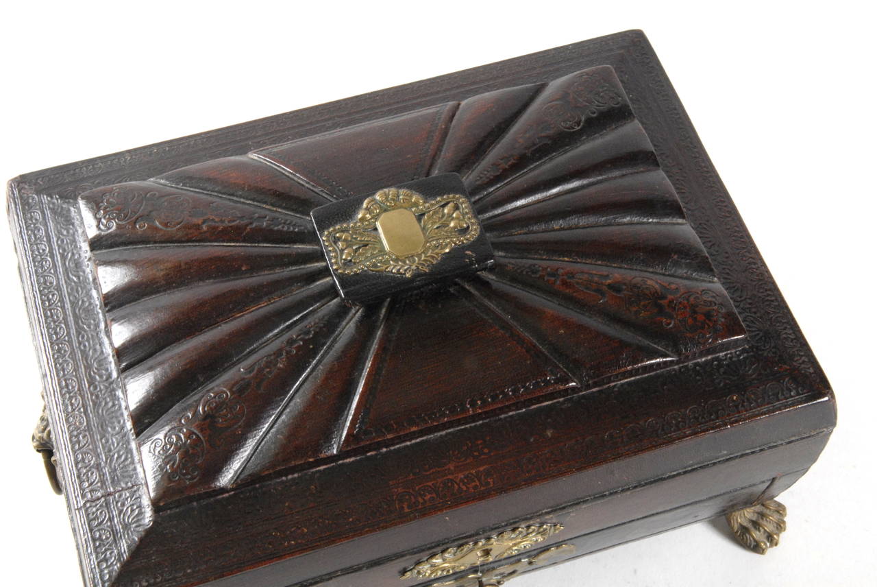 A good shaped sewing box of tooled leather with finely cast brass fittings. Stands on lion's paw feet. The leather is a deep burgundy colour with some minor chipping to corners. The interior is fitted with compartments in blue paper and blue silk,