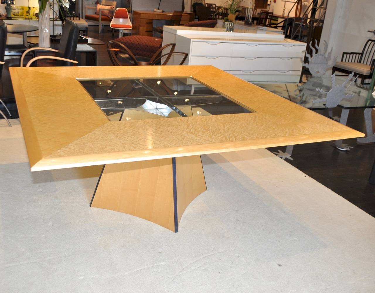 A striking square dining table for eight made from birds-eye maple veneers with polished chrome cross bars supporting a glass topped centre. Made by boutique cabinet makers Senior & Carmichael of Benchworth, England.
