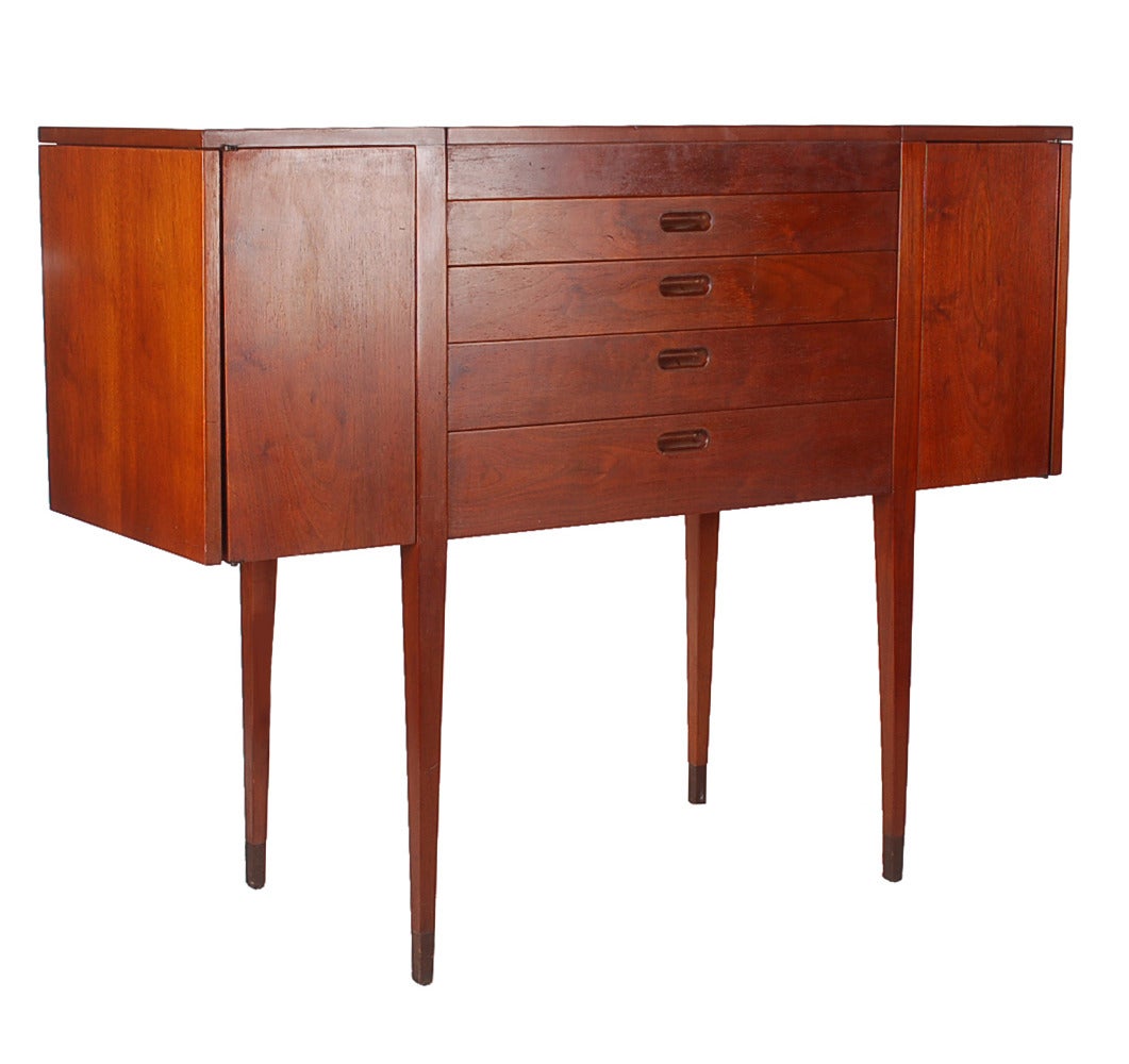 A very stylish tall sideboard made by Dunbar. This 1950s cabinet has many Danish and Scandinavian design elements. Each pop up leaf adds 18 inches in width.