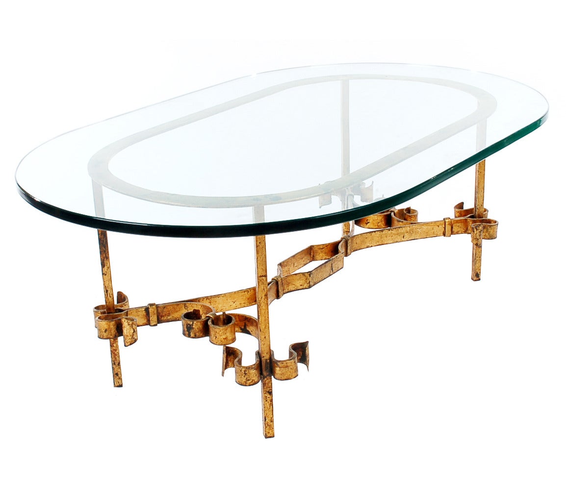 A simple yet ornamental coffee table. It features an extremely heavy gilt cast iron solid base and a thick oval glass top. The table is in excellent all-around condition and showing very light signs of use.