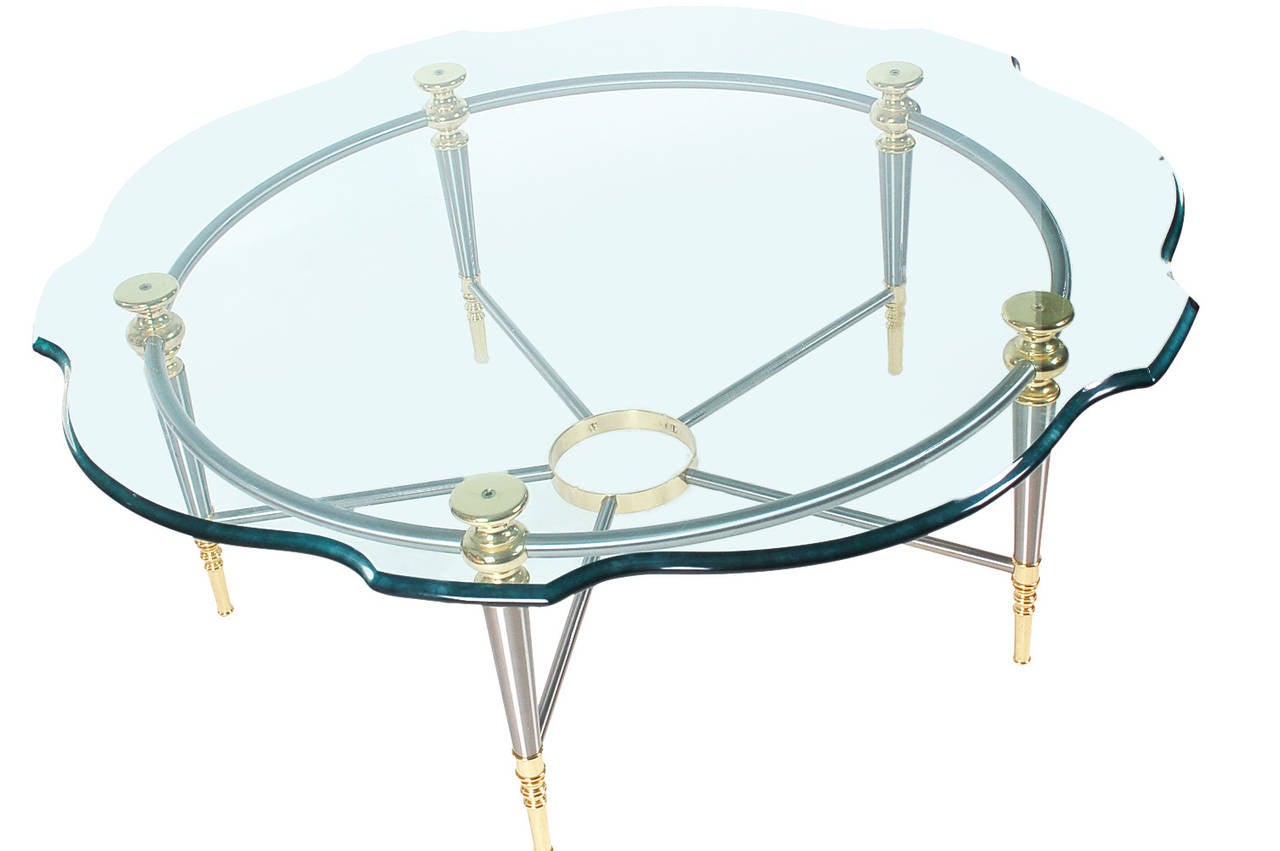 A neoclassical styled coffee table in the style of Maison Jansen. It features a brass and stainless steel base with a heavy scallop cut glass top.