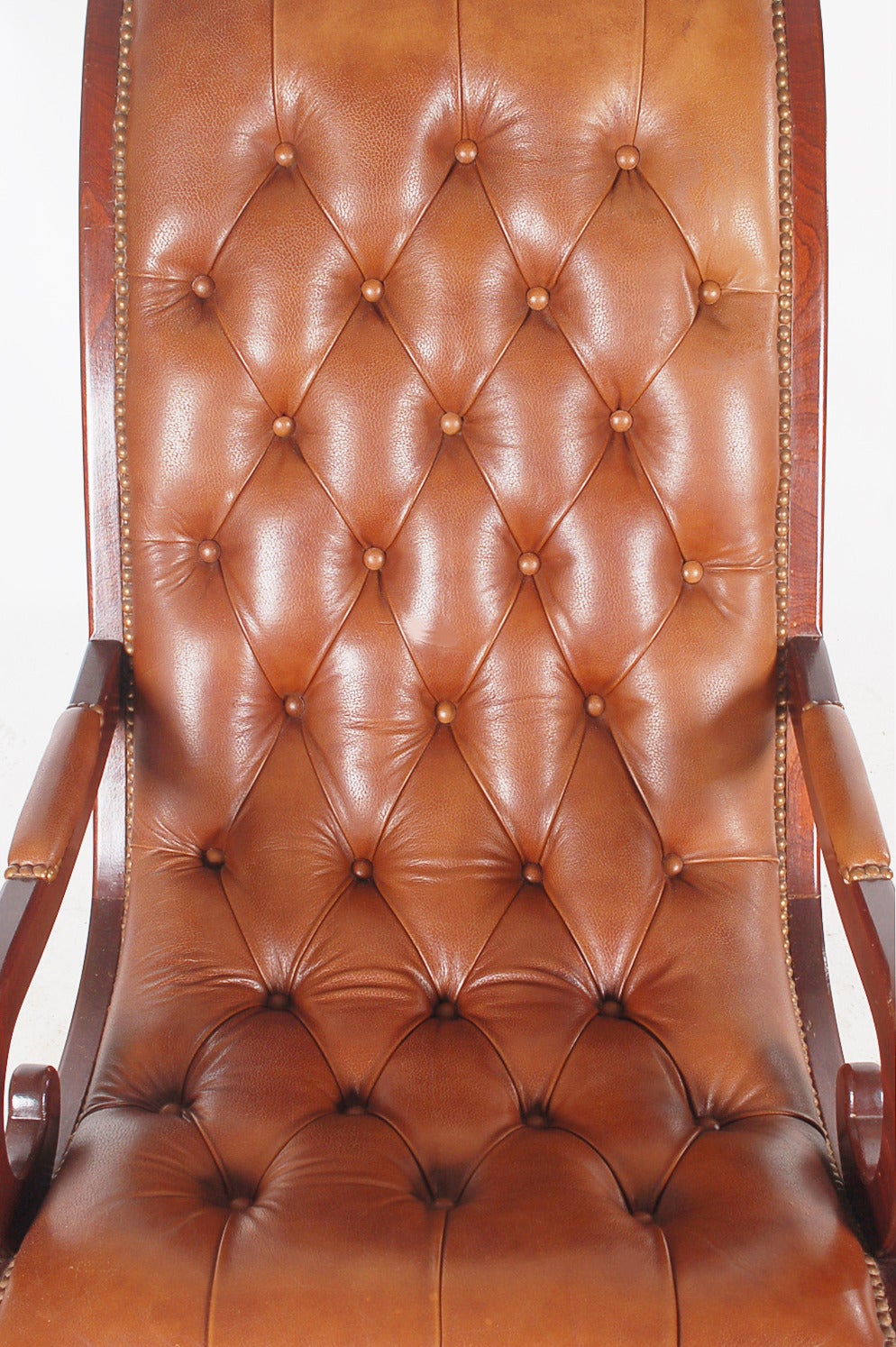 A handsome looking rocking chair full of beautiful details. It features a mahogany wood frame with tufted leather cushioning.