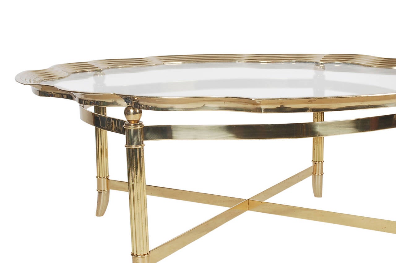A classic looking cocktail table in the style of LaBarge. It features a brass X base and a solid brass framed glass tray top.