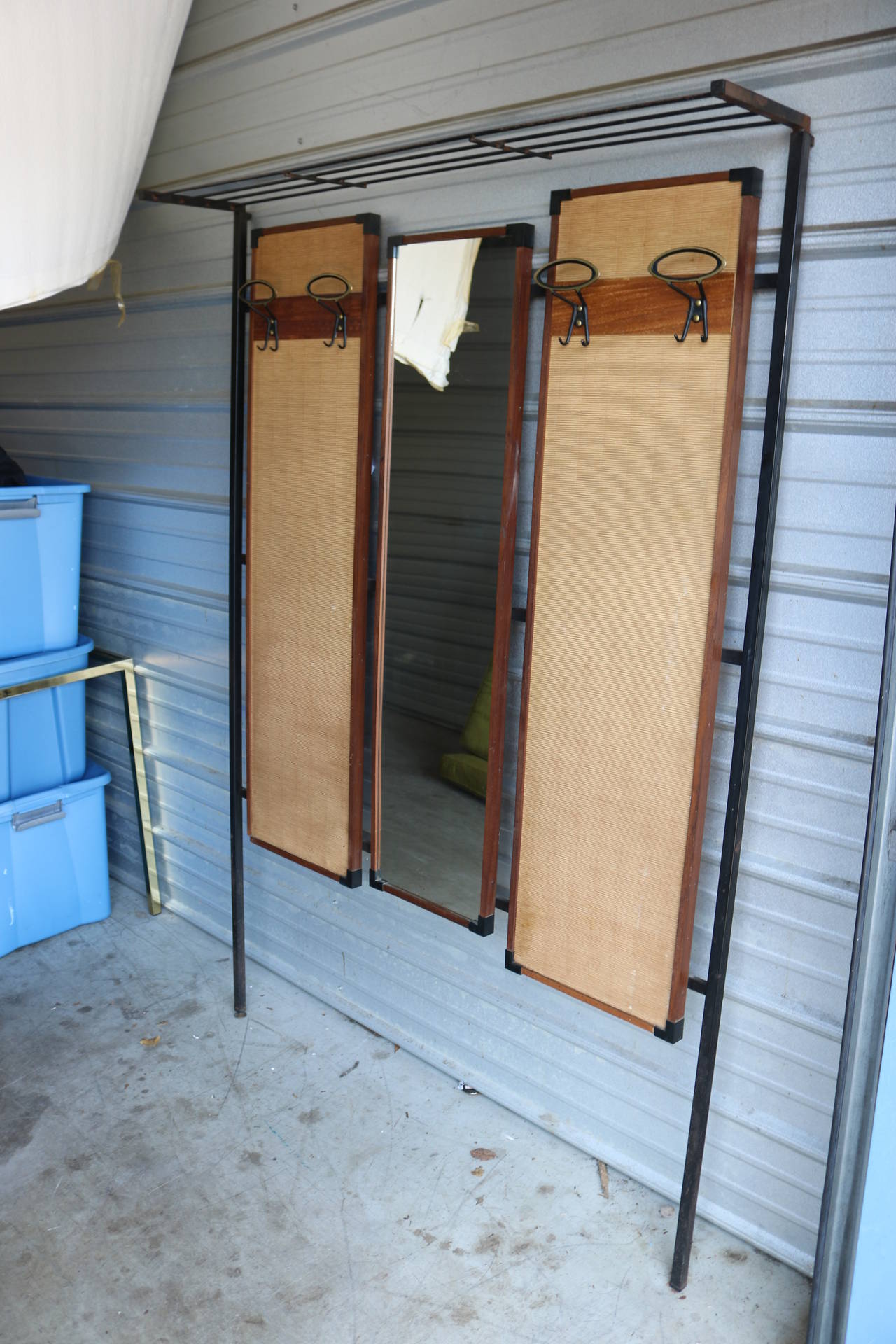 This is a great piece of utilitarian design from Italy. Made in the 1950s, this hall tree is made of iron, glass cloth and brass. Two side panels feature sculptural brass hooks. Middle panel is a mirror. Shelf on top is 12 inches deep. Iron has some