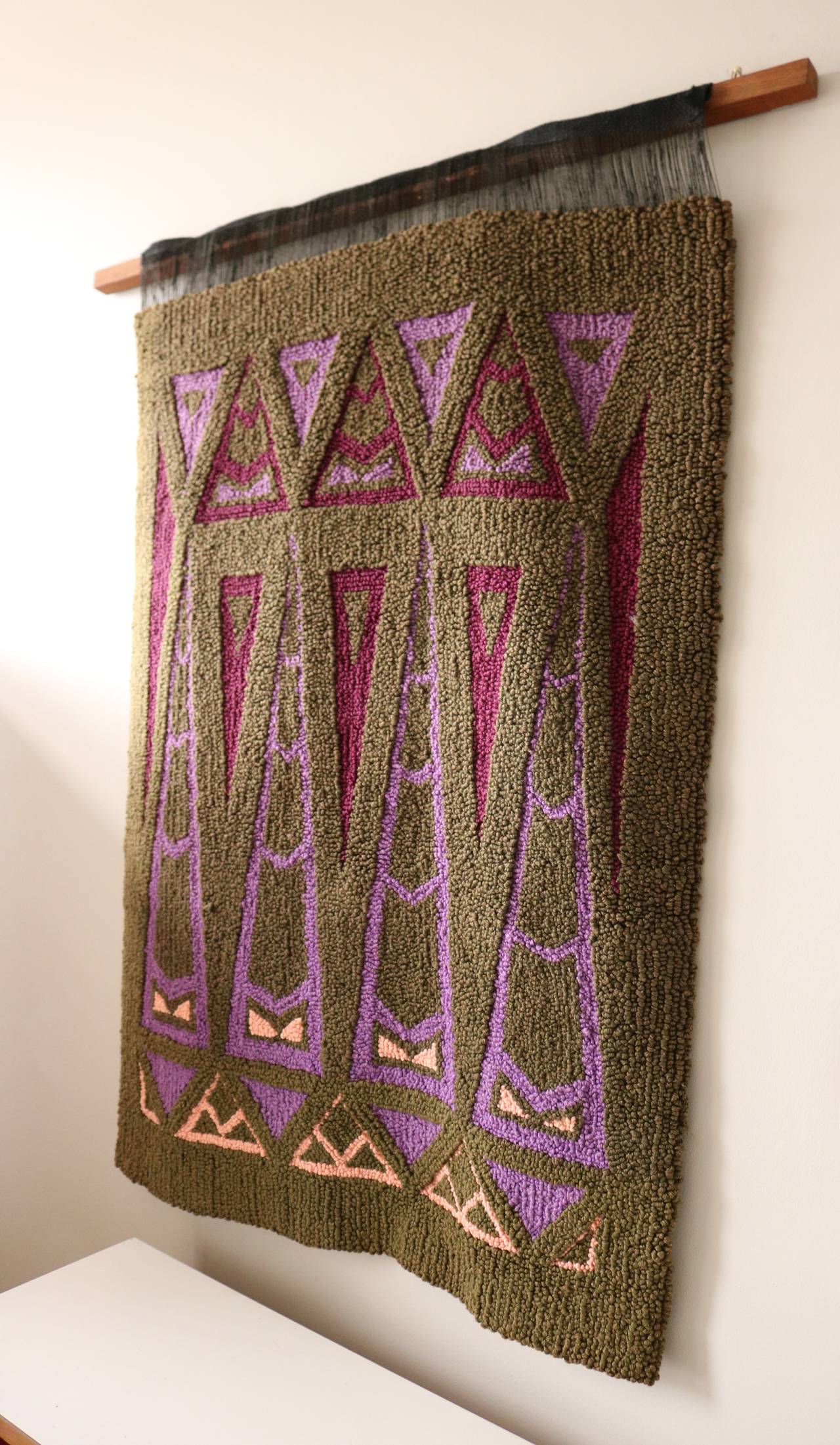 This is a lovely hand knotted fiber art piece by Mamoroneck weaver Beatrice (Betty) Pan.  It takes its cues from art deco motifs and Frank Lloyd Wright windows.  An earthy green background gives way to geometric shapes in wine, lavender and peach. 