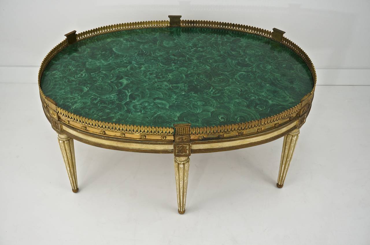 Early 20th Century oval cocktail table in the Louis XVI style.
With tapered fluted legs and apron painted in an antique cream and gold leaf finish. Faux malachite top surrounded by a antiqued brass gallery.

Please feel free to contact us