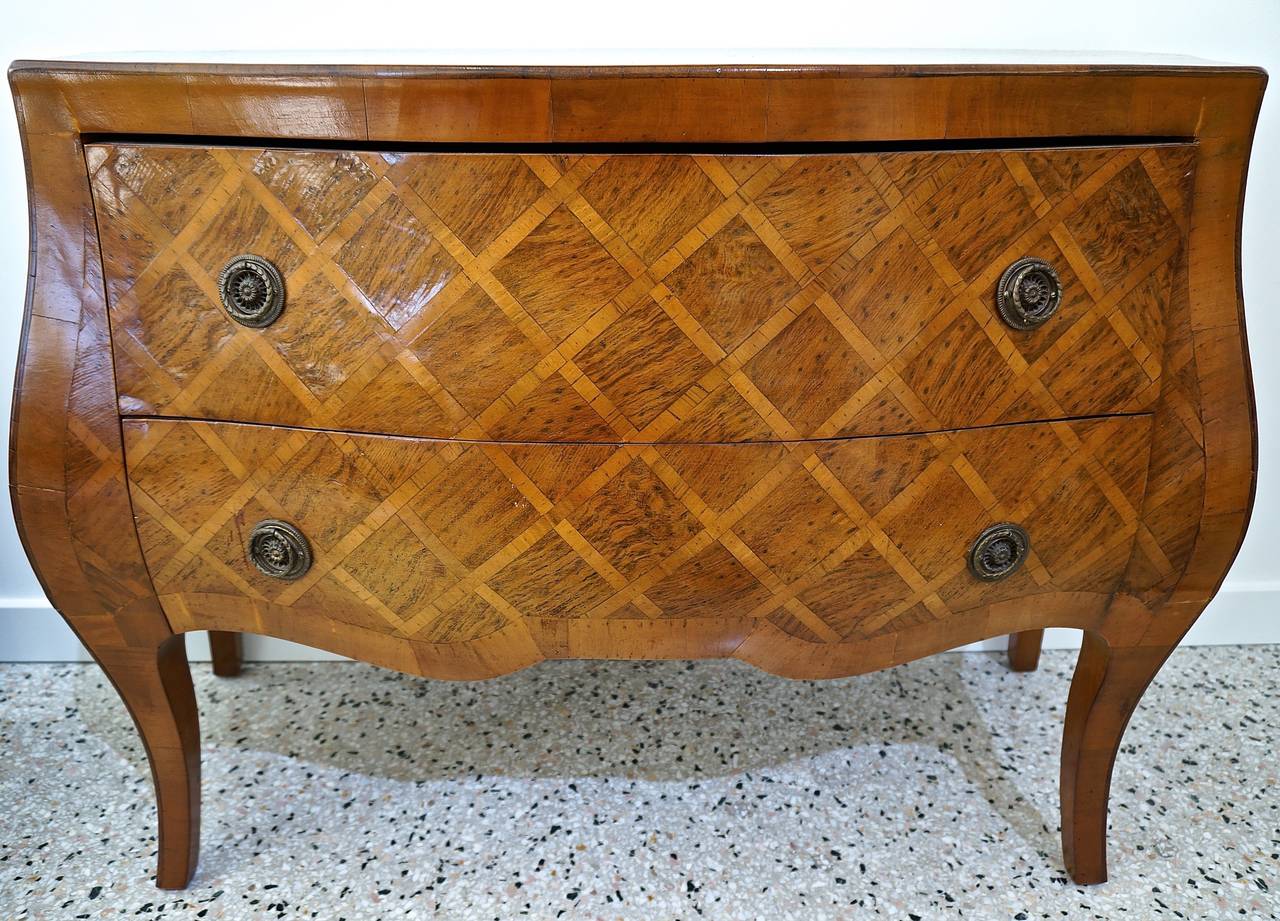This beautiful  Louis XV style Italian commode has the classic diamond-pattern marquetry in three woods all finished in a deep and warm brandy/honey  coloration.  The round handle-pulls are pierced with a rope twist ring and finished in a patinated