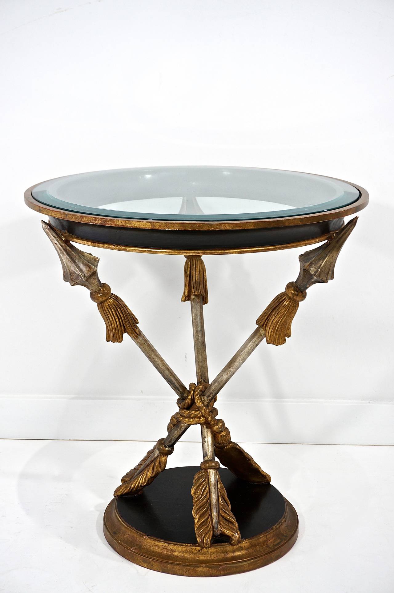 This Italian occasional table with its three crossed arrows bound by a tasseled rope captures the French Empire romantic spirit.  It is hand carved wood that has been finished in antique gold-leaf, silver-leaf and black paint.  The circular top is