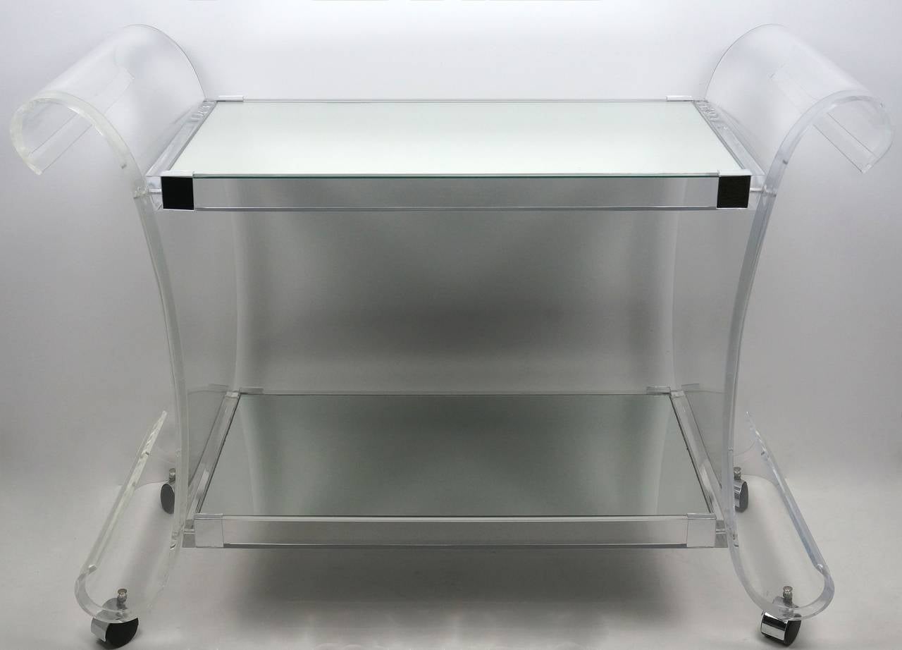 This Lucite bar cart or trolley was designed and produced by Charles Hollis Jones in the 1970s. The con-caved sides give this piece a graceful movement and combined with the two mirrored shelves a very light presence. The casters allow a 360 degree