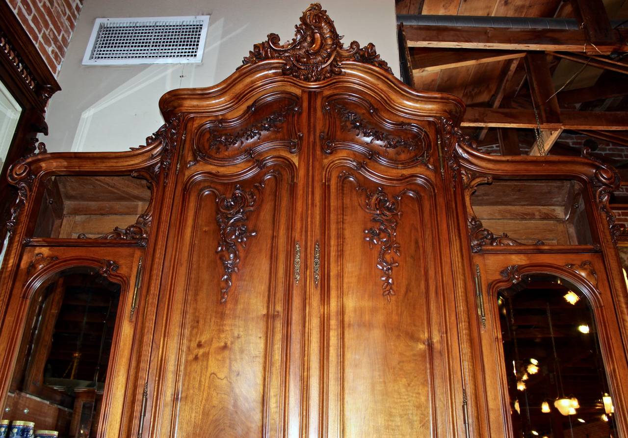 This massive French armoire is made in the Louis XV style from beautifully carved walnut.  The armoire is made in an exquisitely unique size.  Each section of the armoire is accented by gorgeous, hand-carved details.  Storage includes two side