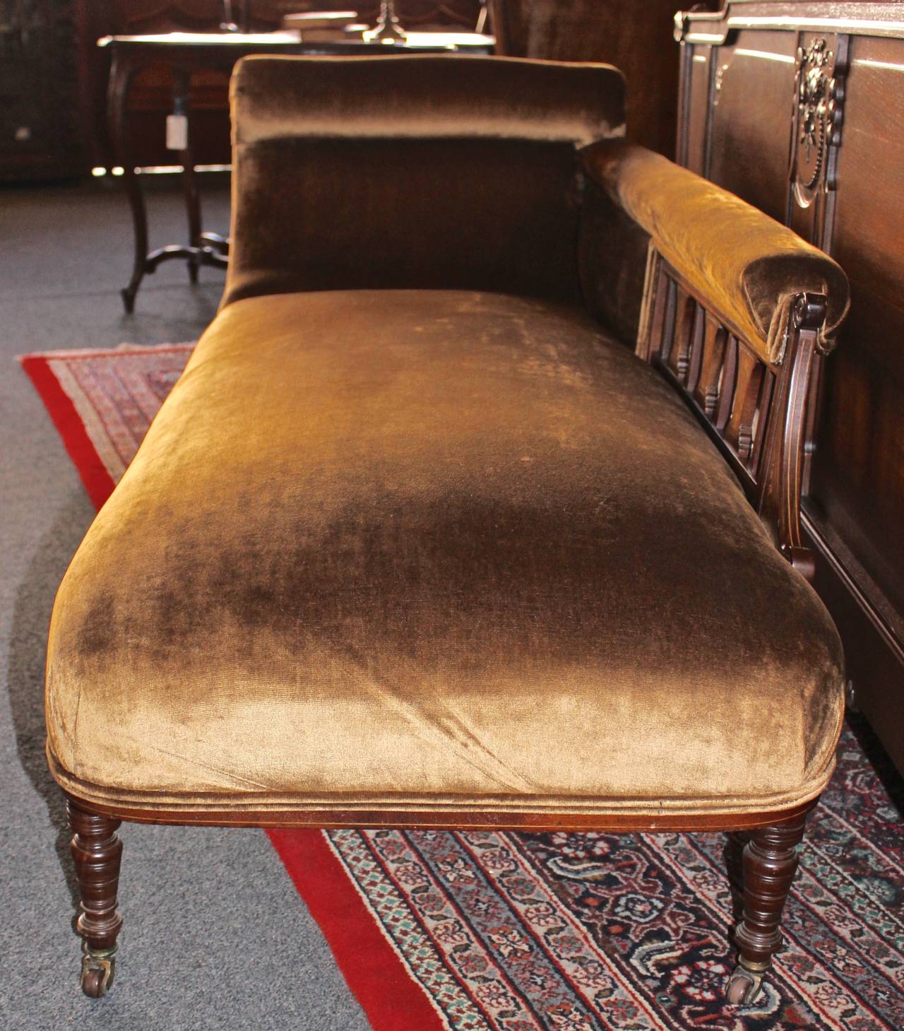 This fainting couch was made in England during the early 1900s. The piece features gorgeous, inlay detail and a plush upholstery.  The fainting couch has casters on all four wheels.