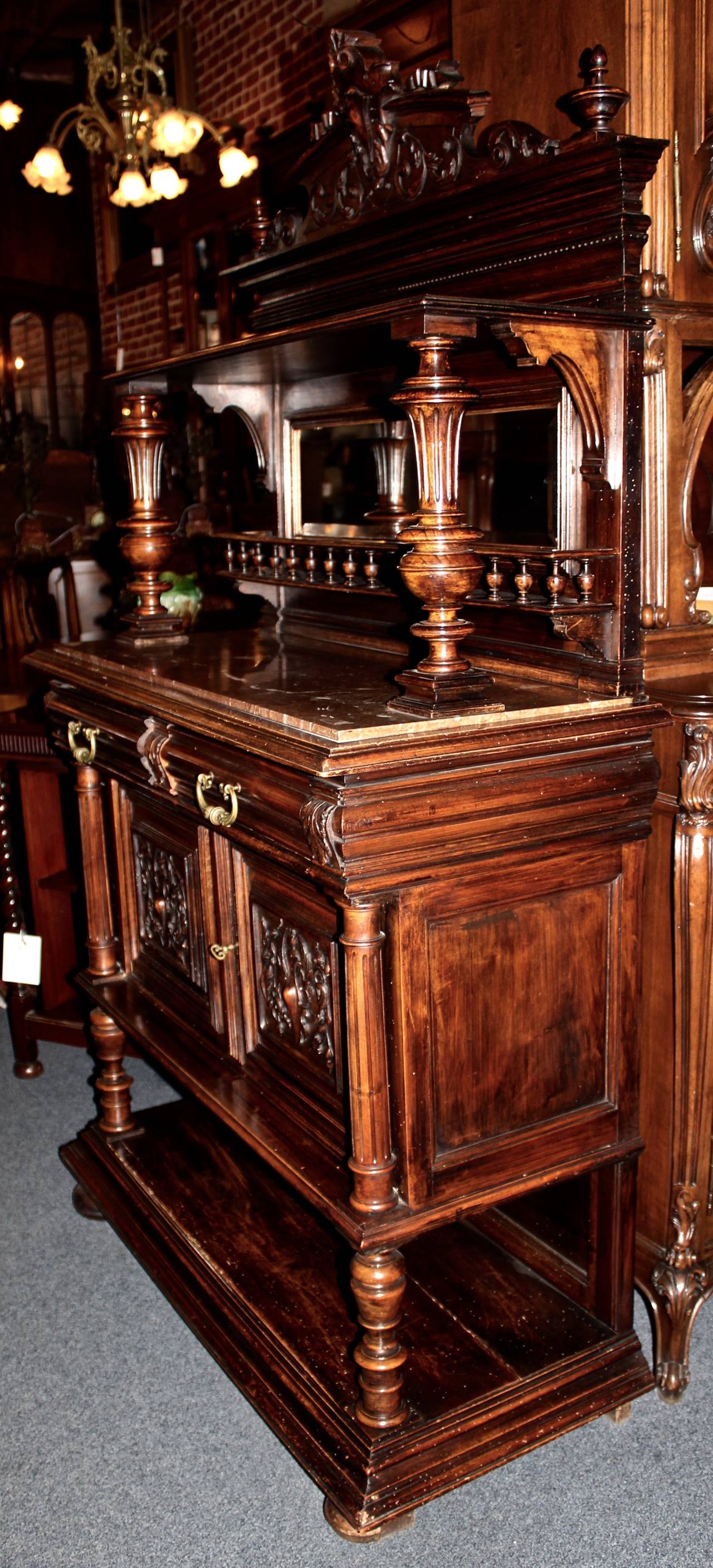 This French server is made in the Henry II style from walnut.  The piece is ornately carved with details suggestive of the style.  It features a marble top with a mirror above it.  Storage includes two pull-out drawers, two swing doors with