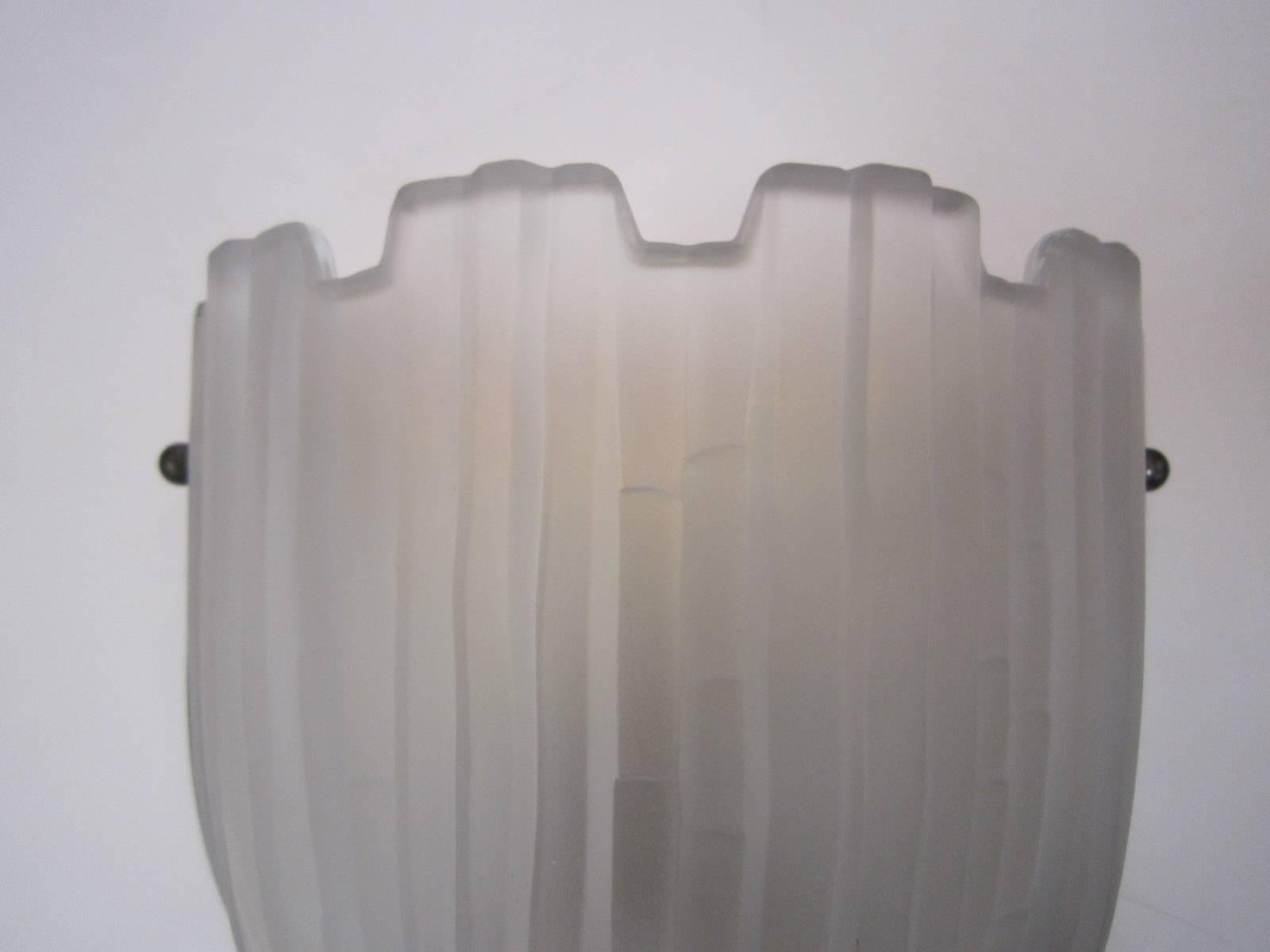 A single French frosted art glass wall sconce by Sabino with linear pattern overall, mounted on matching shaped heavy nickeled bronze backplate with stepped pattern. The top of the sconce bears a semblance to the design of a fortified city wall.