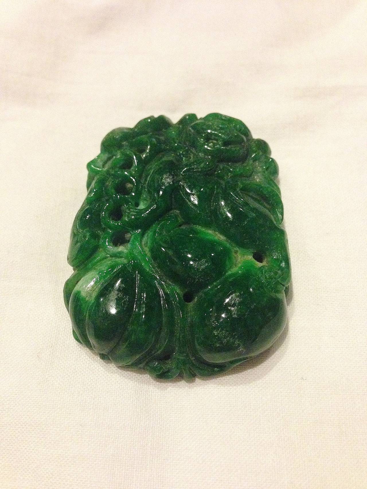 This splendid, 52.1 gram, glossy green jade piece features exquisite full carvings. A foo dog occupies the top right corner residing over gourd and pumpkin, the three symbols for 