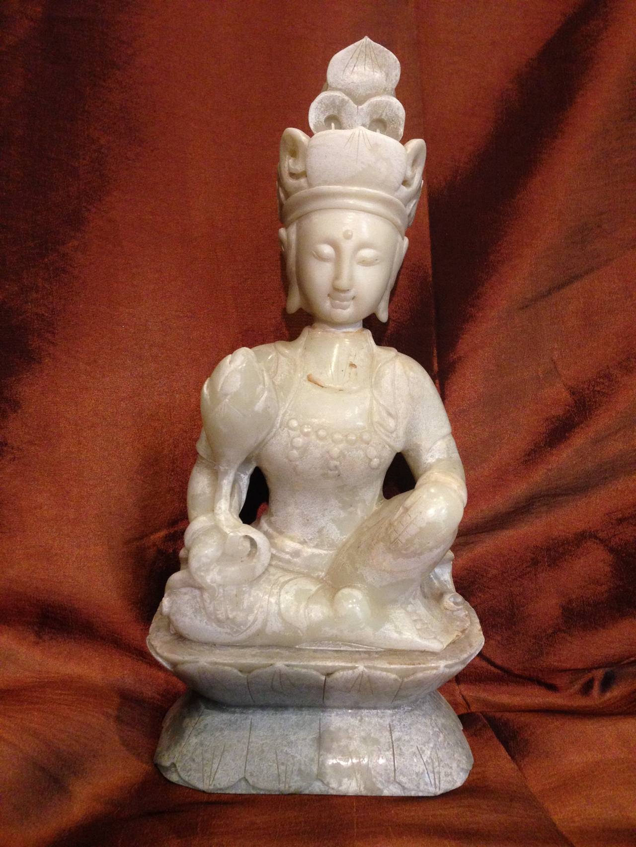 This beautiful sculpture features Buddha with the most serene face. He holds a single lotus which symbolizes peace and harmony. 

This piece has an artistic design that is unique to white Jade sculpture. The artist chose to incorporate a thin