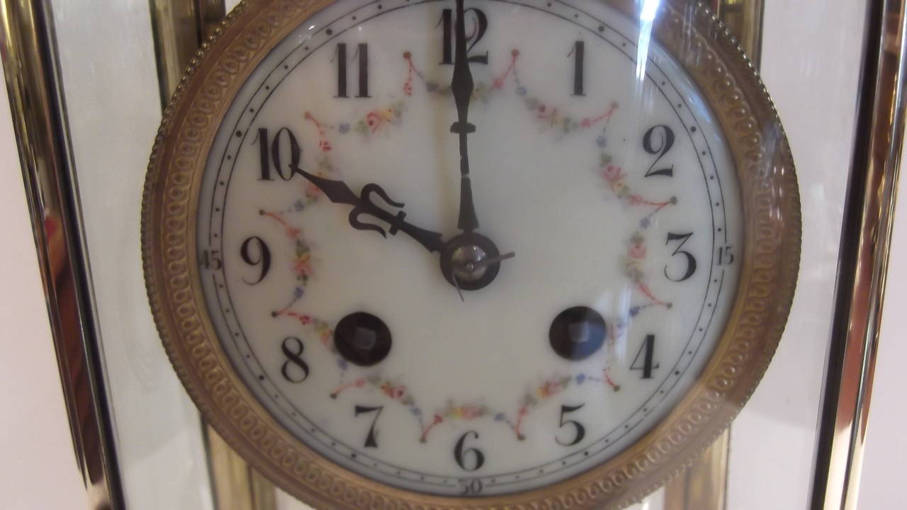 An oval French crystal regulator clock with beveled glass. 
Polished brass body with oval form fitted with curved glass panels.
The face is painted with garlands of flowers and leaved, very delicate.
The clock gongs softly on the hour and half