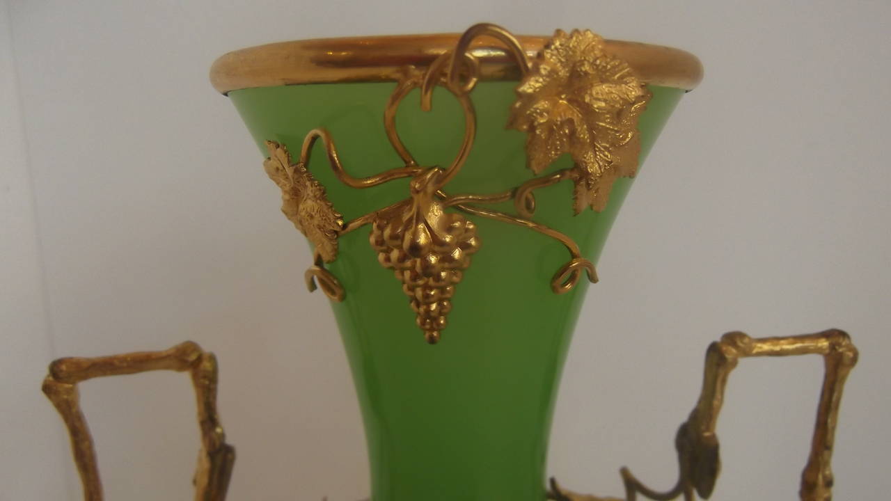 A gorgeous French 19th century opaline vase, in a rare apple green color.
The glass is mouth blown with a polished pontil on the base. The body and base are encased with gilt grape vine pattern mounts. The wire vines have grape leaves and grape