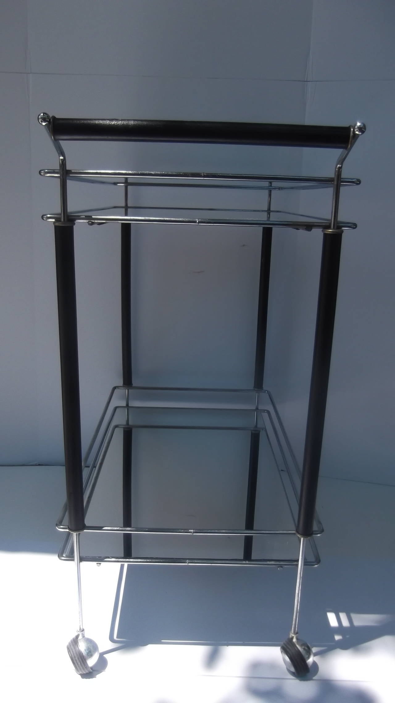 A neat rectangular two tiered cart with castors.  The shelves are mirrored rather than glass which give it a sleeker look
The chrome frame is accented with ebonized wood on the four corners and handle.  Perfect smallish size and  very usable for