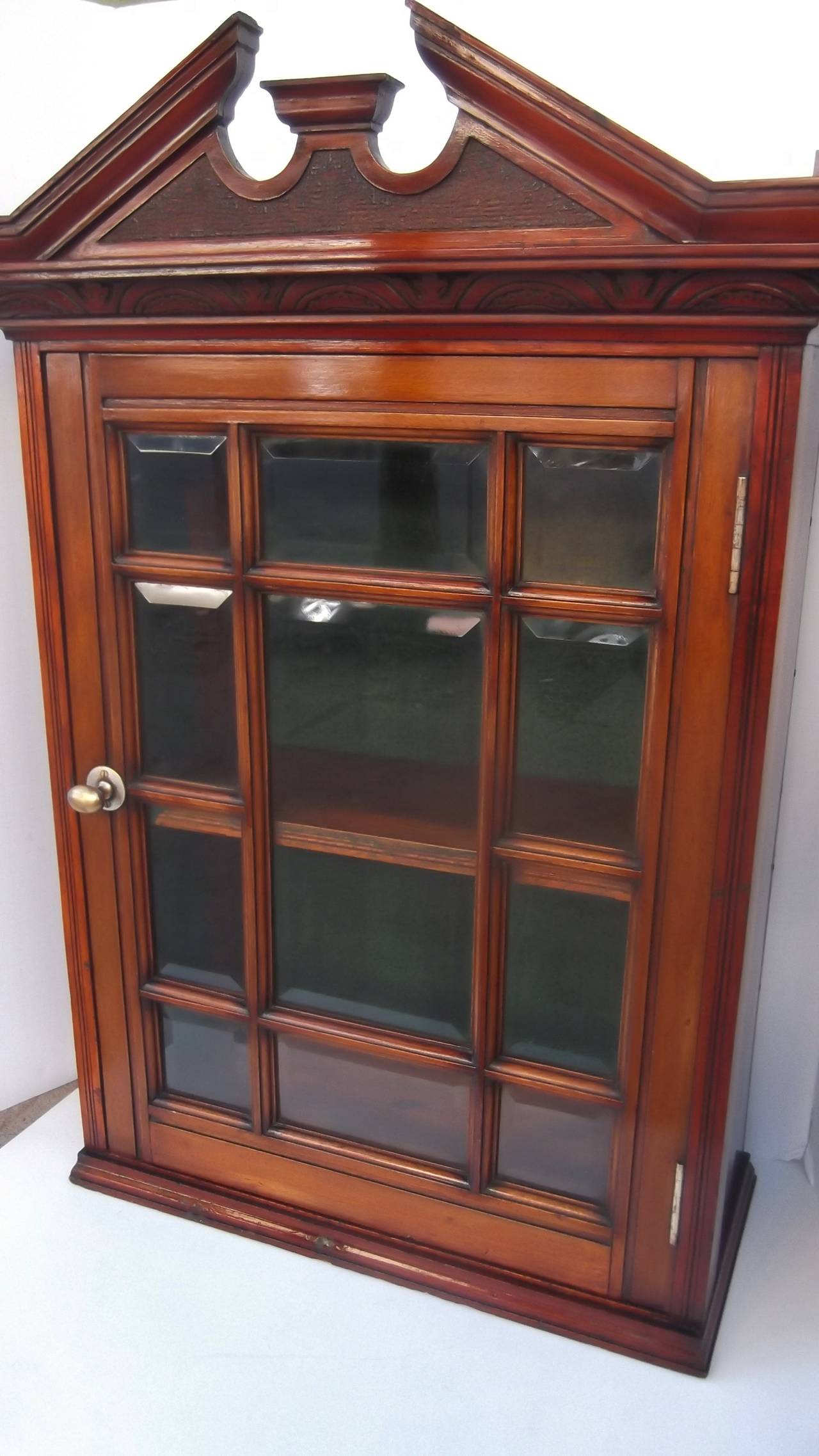 A fine mahogany portable curio cabinet with hand beveled individual glass panels. Classic Georgian style pediment top with carved detailing.  This can also hang on a wall by the added sturdy metal braces.  The display area has 2 wood shelves.