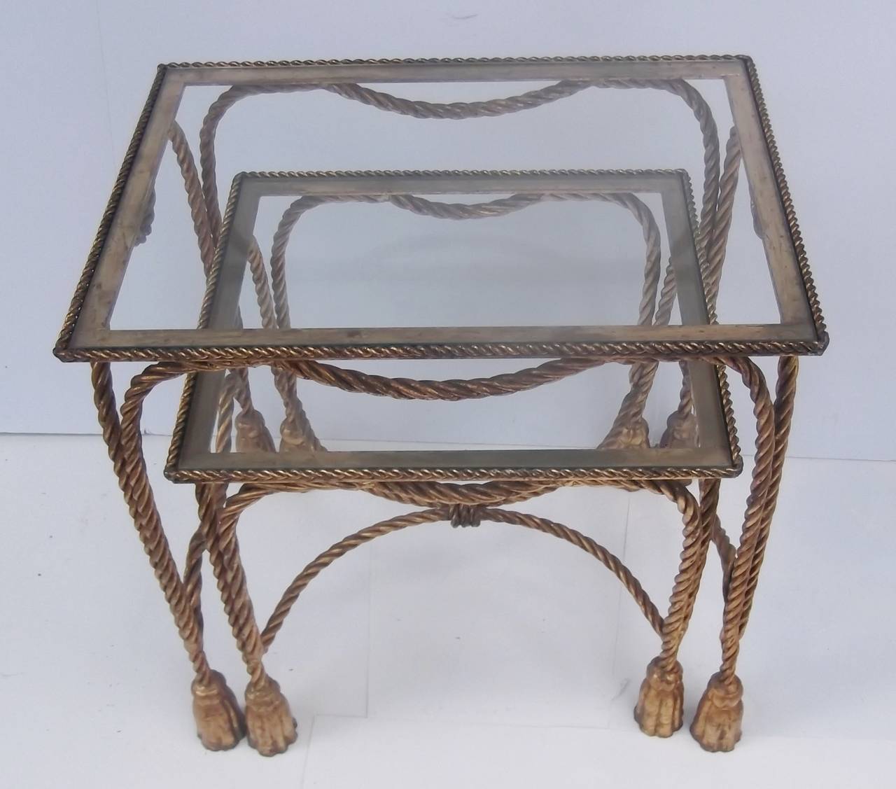 Made in Italy, these are a nice set of whimsical nesting tables with glass tops.
The frames are rope style gilded iron with fitted glass top inserts all resting on tassel motif feet. This was a poplar style in the 1950-1960 and tables, chairs and