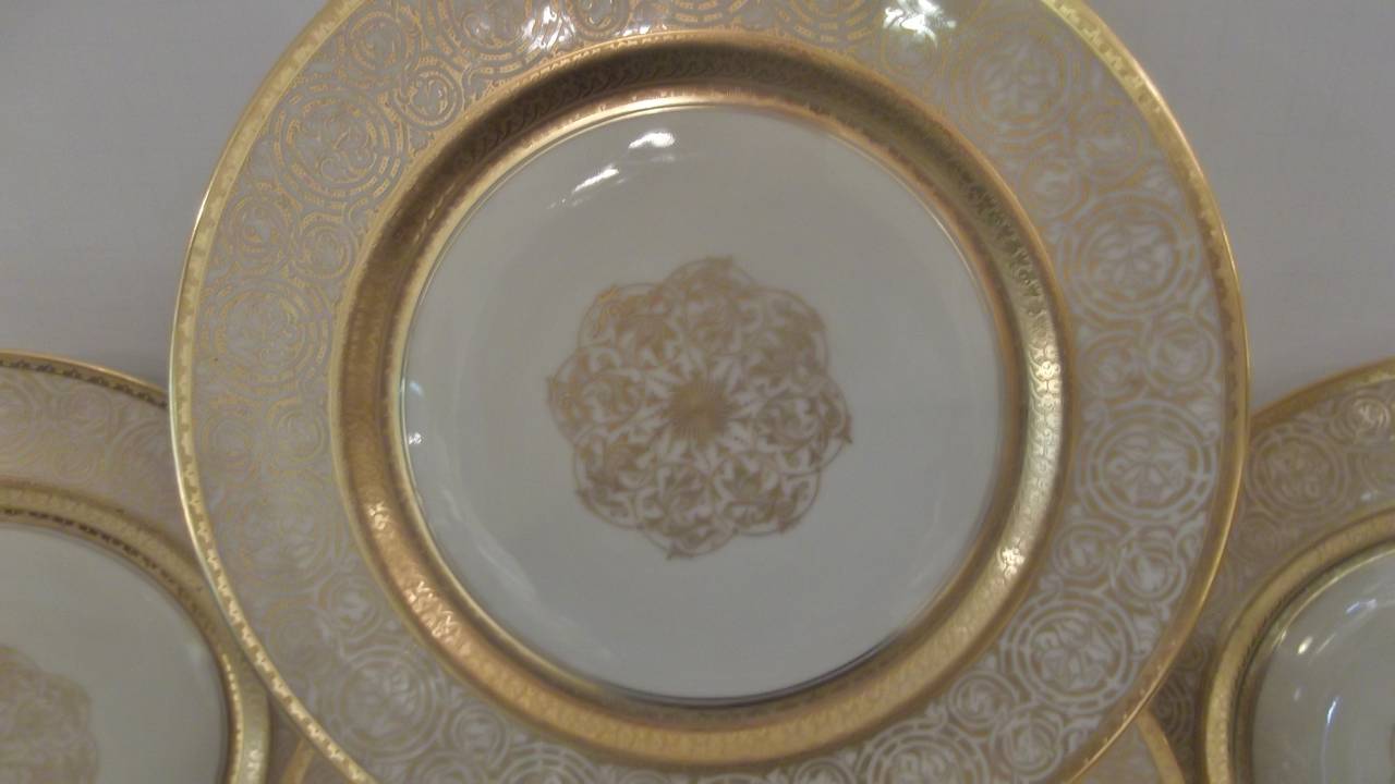 A set of 15 service plates or chargers in unused condition. Thick and detailed borders with a filigree center medallion. A clean off-white background is set apart with luxurious gold decoration and a full 11