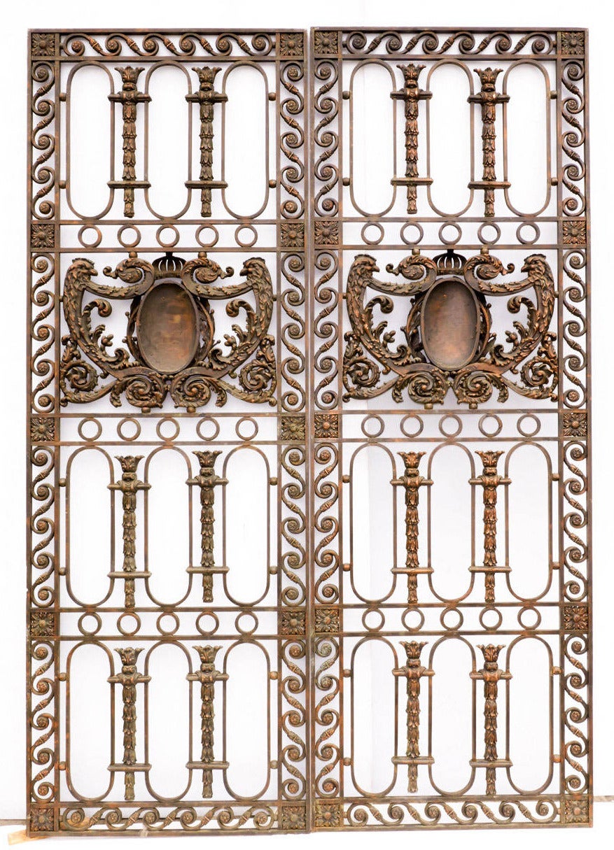 Pair of stately early 20th century Beaux Arts style door panels. Finely crafted wrought and cast-iron details include running scrollwork border, rosettes, garlands, and large central cartouche motifs.  Panels have double sided ornamentation and can