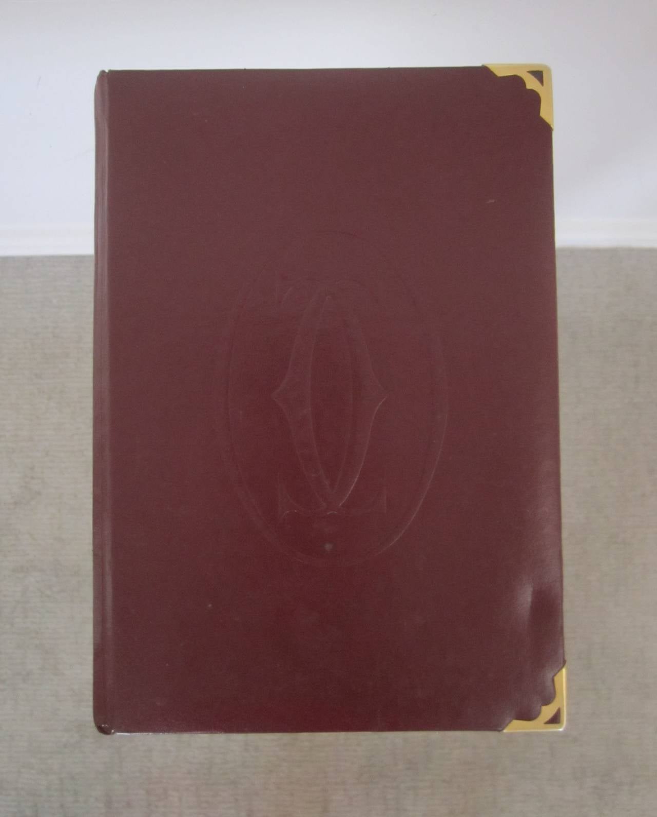 Vintage Cartier les must de Cartier Book by Assouline. 
Book is perfect bound in the classic Cartier burgundy color, brass tips on corners, embossed Cartier C on front, and gold leafing on ends of paper. Circa 2002.