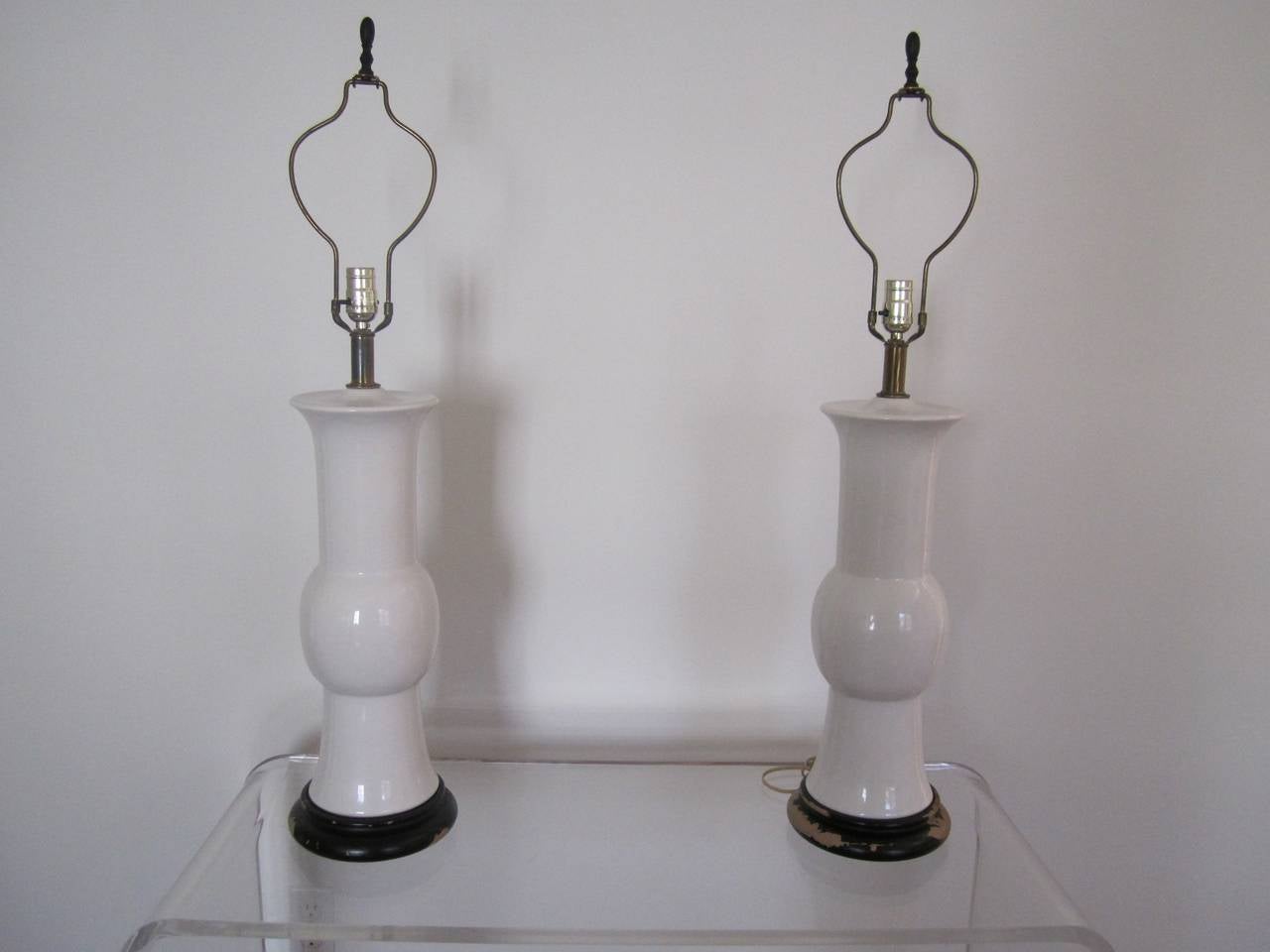 A stunning pair of vintage tall white 'blanc-de-chine' table lamps with original black wood bases and black metal turned finials, in the style of James Mont, circa 1960s.

Measures: 21 in. H to top of lamp base, or 29 in. H to top of original black