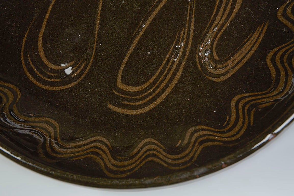 A studio pottery bowl by Michael Cardew from his time at the Abuja Pottery in Nigeria, where Cardew taught local craftsmen. His work from this period often incorporates African style designs. This stoneware bowl is glazed in a rich dark brown slip,
