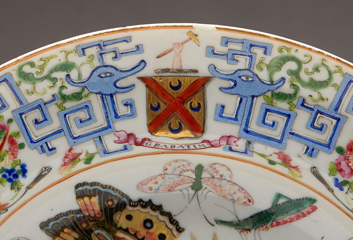 An antique Chinese Qing shallow bowl shaped porcelain plate finely and extensively hand-painted in the famille rose palette with butterflies and insects within a stylized dragon and Greek key patterned border with floral baskets and with two coats