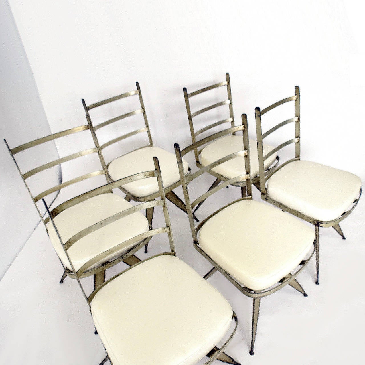 Stunning set of six dining chairs that swivel. Torch cut metal is silver leafed and has some age and patina. Seat cushions are upholstered in off-white vinyl. Could be use indoors or outside in a covered area.