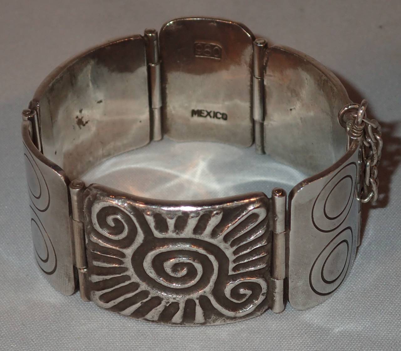 A substantial silver pane and hinge style cuff bracelet with pin latch closer by William Spratling. Formed alternating etched and repoussed panes featuring the swirl glyph design with alternating multi-ring circles motif, clasped together with a