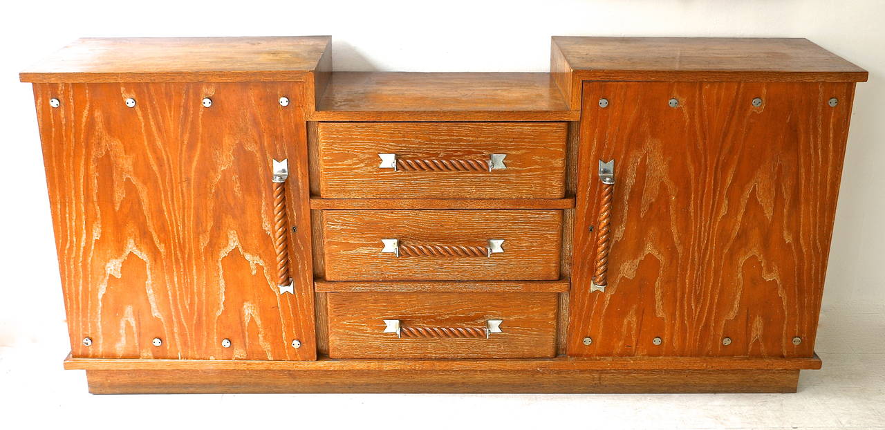 Three parts sideboard tripartite with cubic trunk in oak veneer. It opens in the center by three bunk drawers flanked by two side doors. The handles are in twisted wood, they are held by chrome metal fasteners. 1930s French work.