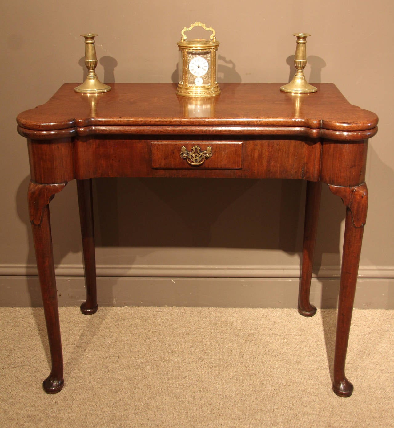 A fine example of a George II red walnut pad foot card table with lappet carved legs and a single drawer to the frieze. The base lined interior has counter trays, circa 1740. 
Shown with engraved oval carriage clock with alarum, circa 1885 £3,850.