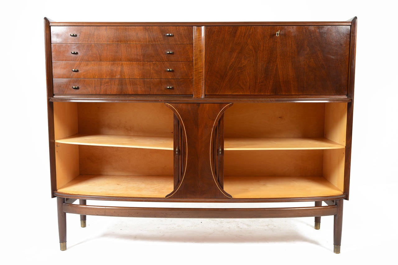 This tall mahogany credenza with tambour doors is a beautiful example of early Danish modern design. The case bows in the front for a beautiful silhouette. The top left cabinet features four drawers with brass pinch pulls. The right door unlocks and