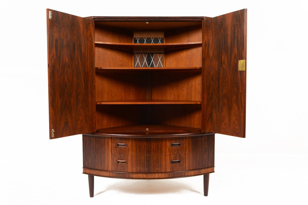 This beautifully understated bow front corner unit in Brazilian rosewood will easily become the new focal point of any room. Two front doors open to a mirrored bar interior. Two top fixed shelves and removable bottom shelf provide ample storage for