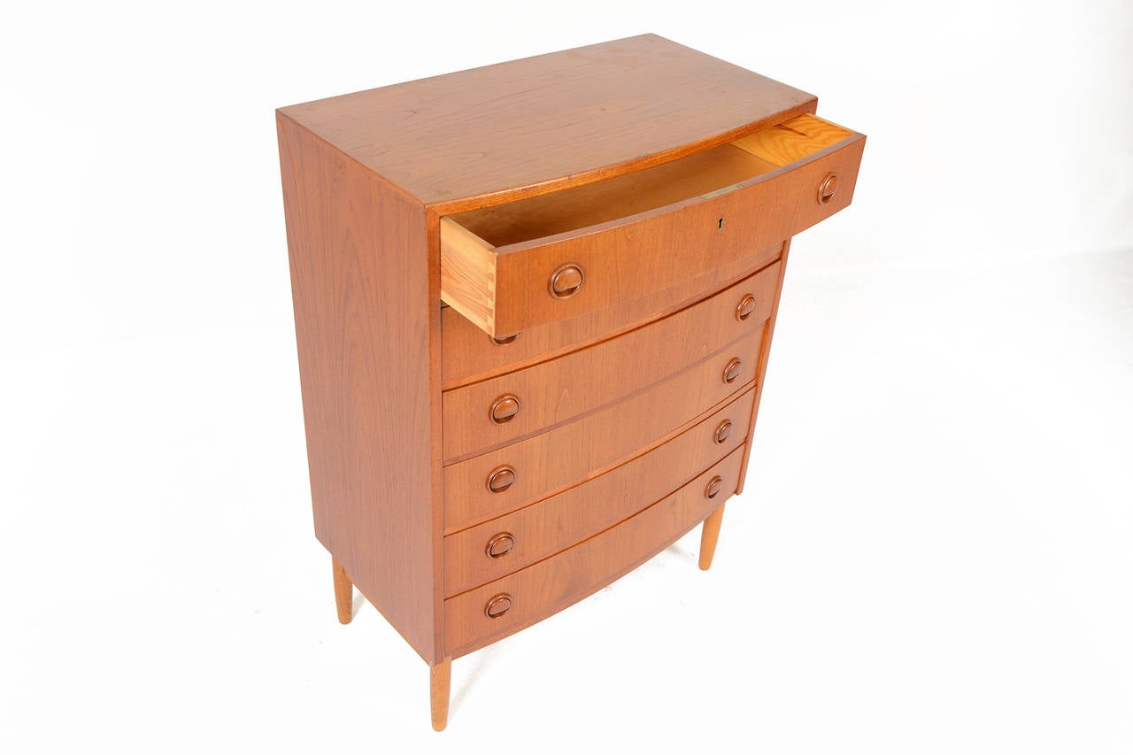 This gorgeous Danish modern mid century bow front teak highboy was designed by Kai Kristiansen in the 1960s and features six wide drawers accented by the designer's signature circular pulls. Stunning turned oak legs support this piece. In excellent