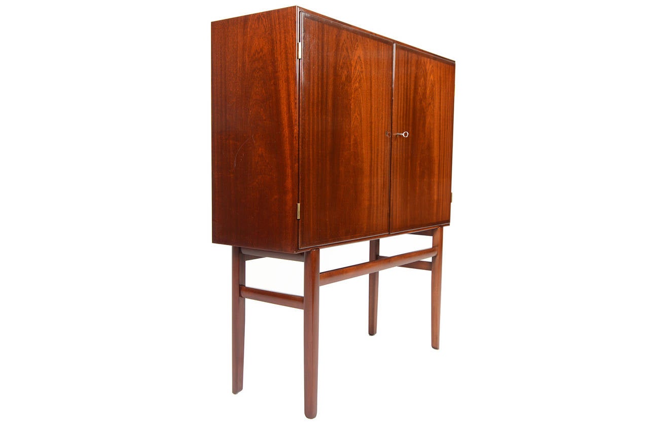 This beautiful tall Danish modern bar was designed by Ole Wanscher for P Jeppesen Møbelfabrik. Two wide doors open to reveal two bays with adjustable shelves. Original key unlocks the doors and allows for a striking flush finish. The tall carved