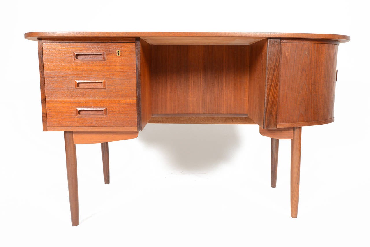 This rare Danish modern atomic mid century teak writing desk offers exquisite vantage points from every angle. This piece features a tambour door bar compartment with a single fixed shelf. The left bank of three drawers provides additional storage.