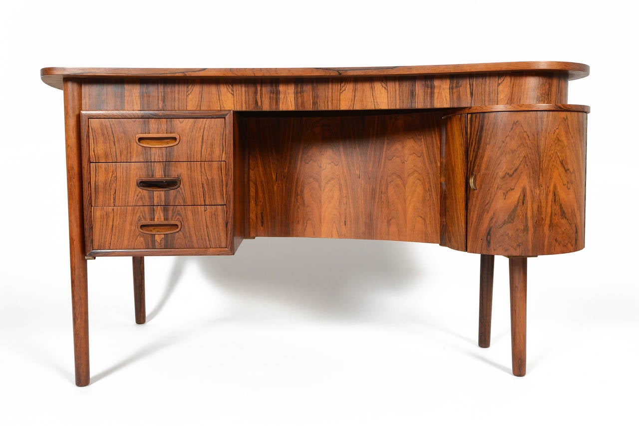 This rare Danish modern atomic mid century Brazilian rosewood writing desk offers exquisite vantage points from every angle. This piece features a bar compartment with a single fixed shelf. The left bank of three drawers provides additional storage.