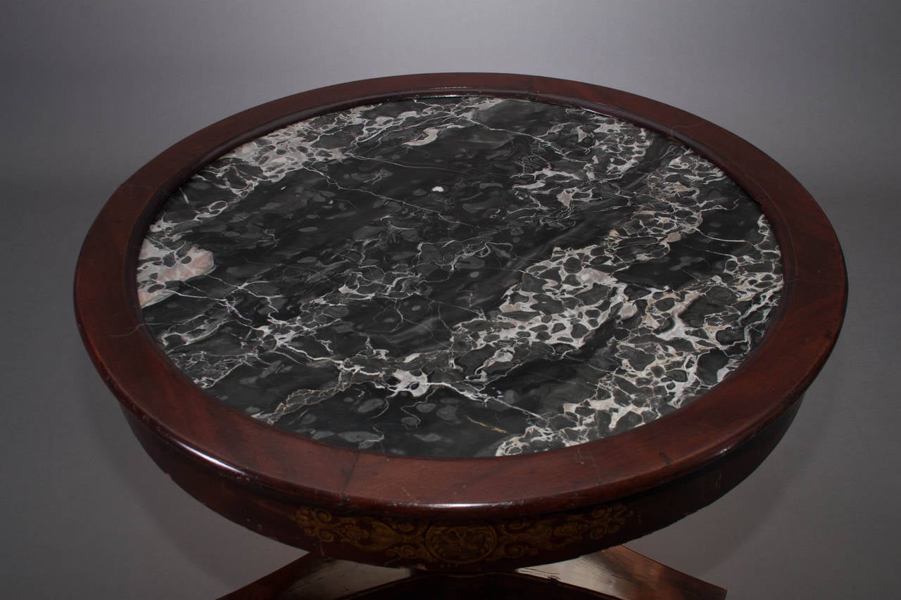 With figured marble inset top,
New York, circa 1825.

The circular top with dark figured marble inset held by a wood frame, above a conforming apron with three large foliate gilt-stencils centering a lion's mask, above a tapering cylindrical