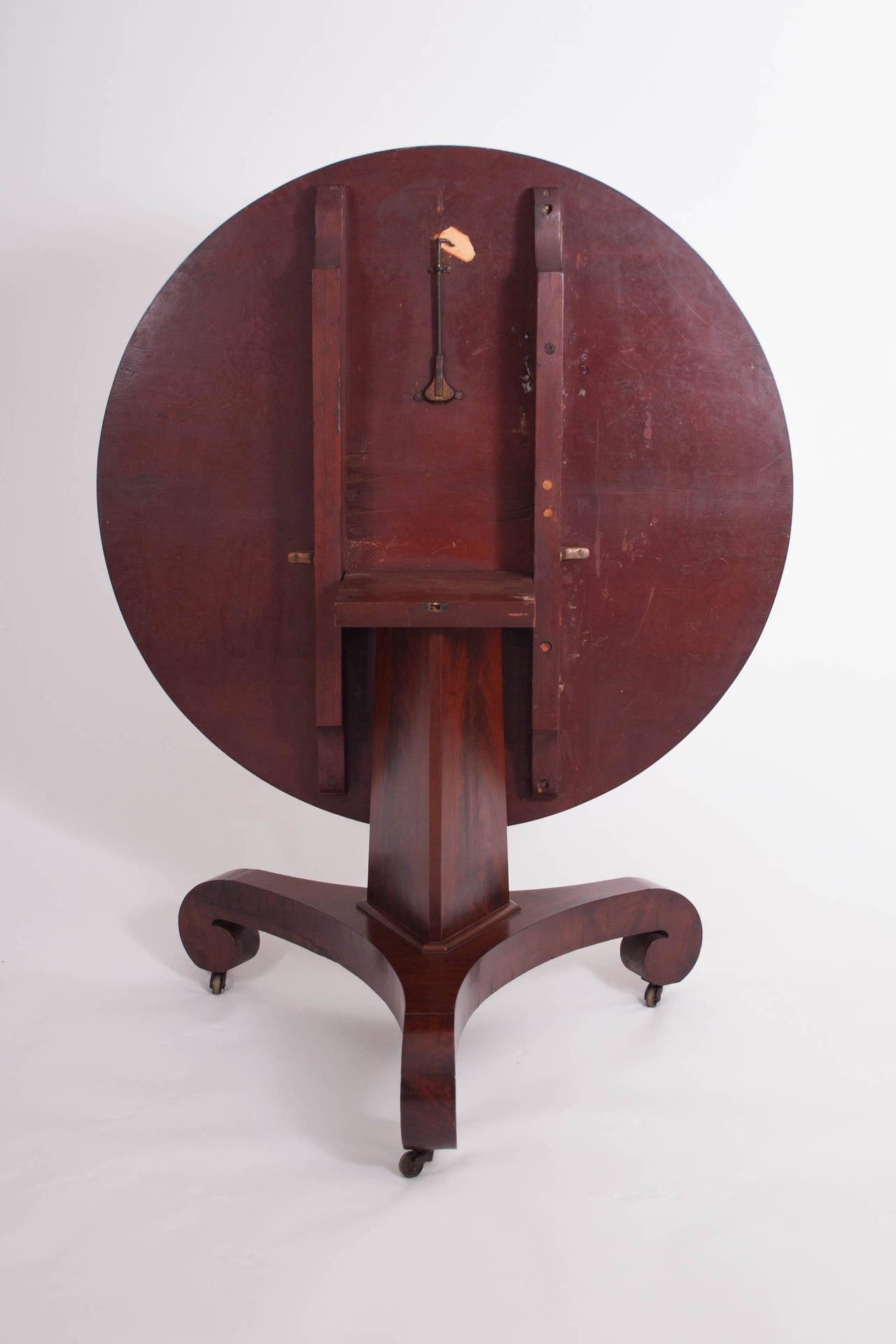 American, circa 1830-1835.

The circular top with pie-slice-shaped flitches for flame mahogany radiating from a central point above a tapering three-sided pedestal faced with flame mahogany veneers on a tripartite base with scrolled feet on