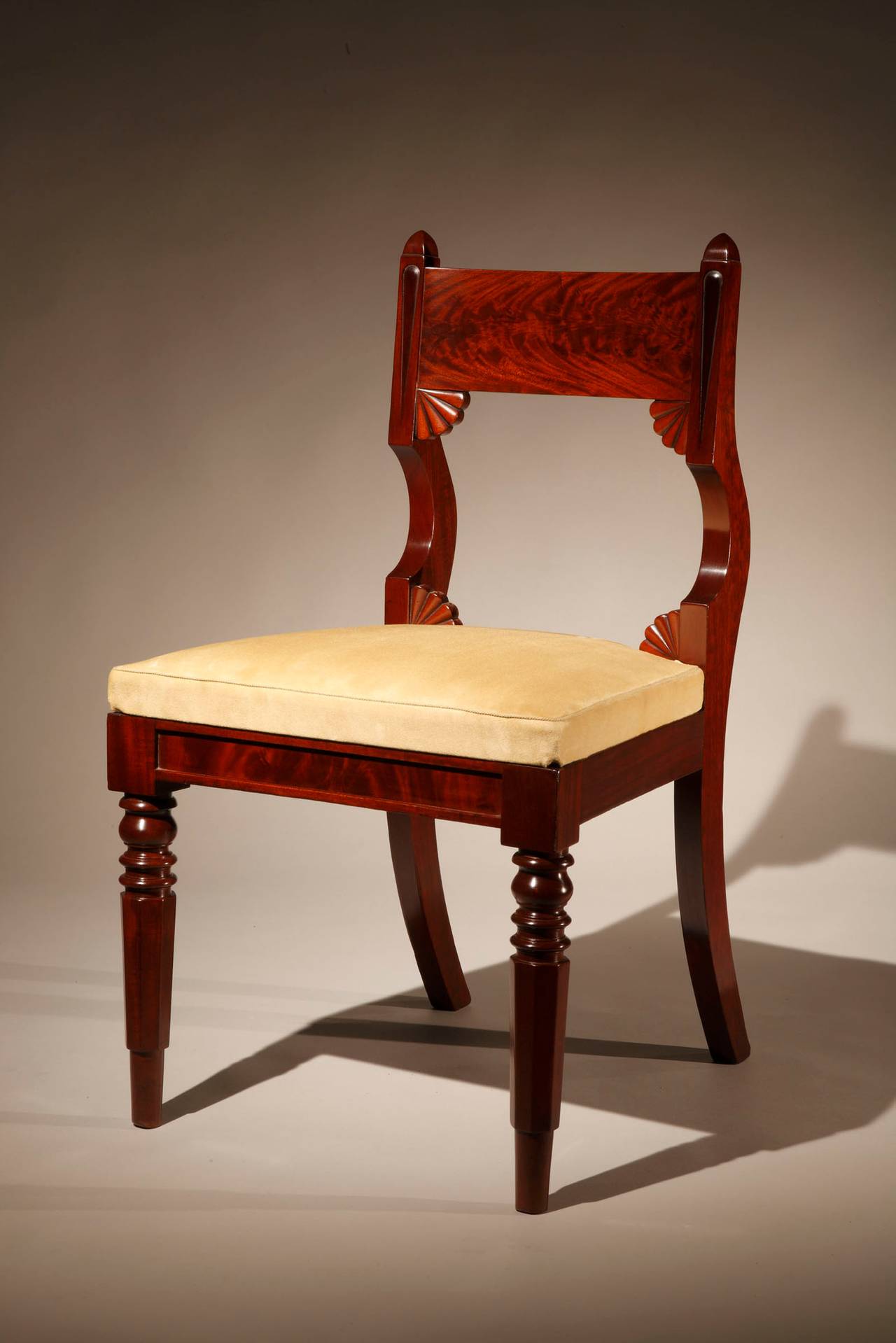 Comprising 11 side chairs and an armchair,
Philadelphia, circa 1830.

The slightly curved tablet crest rail held between incised styles with pyramidal tops and distinctively curved-back above the upholstered slip seat and continuing as saber rear